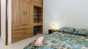 Une chambre à coucher avec une armoire en bois, un lit recouvert d’une couvre-lit à motifs floraux et une lampe de chevet.