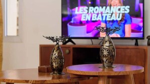 Un téléviseur diffusant l’émission « LES ROMANCES EN BATEAU », avec deux vases décoratifs posés sur une table en bois.