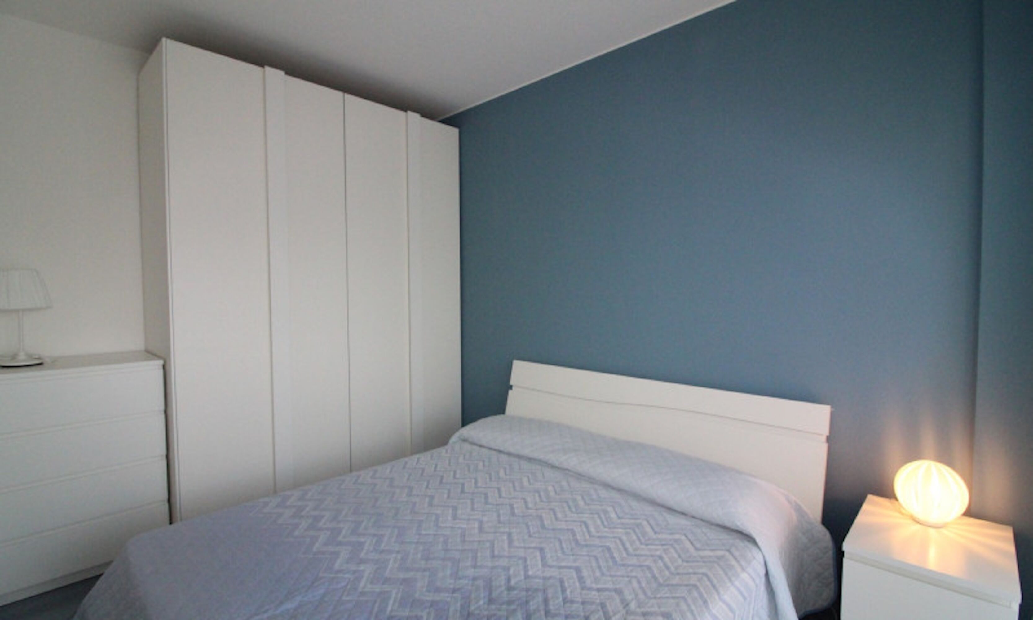 A bedroom with a bed, a nightstand with a lamp, and a wardrobe.