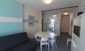 A compact living space with a dining area, a sofa, and a kitchenette. - Modern Flat With Pool View (Lignano Sabbiadoro)