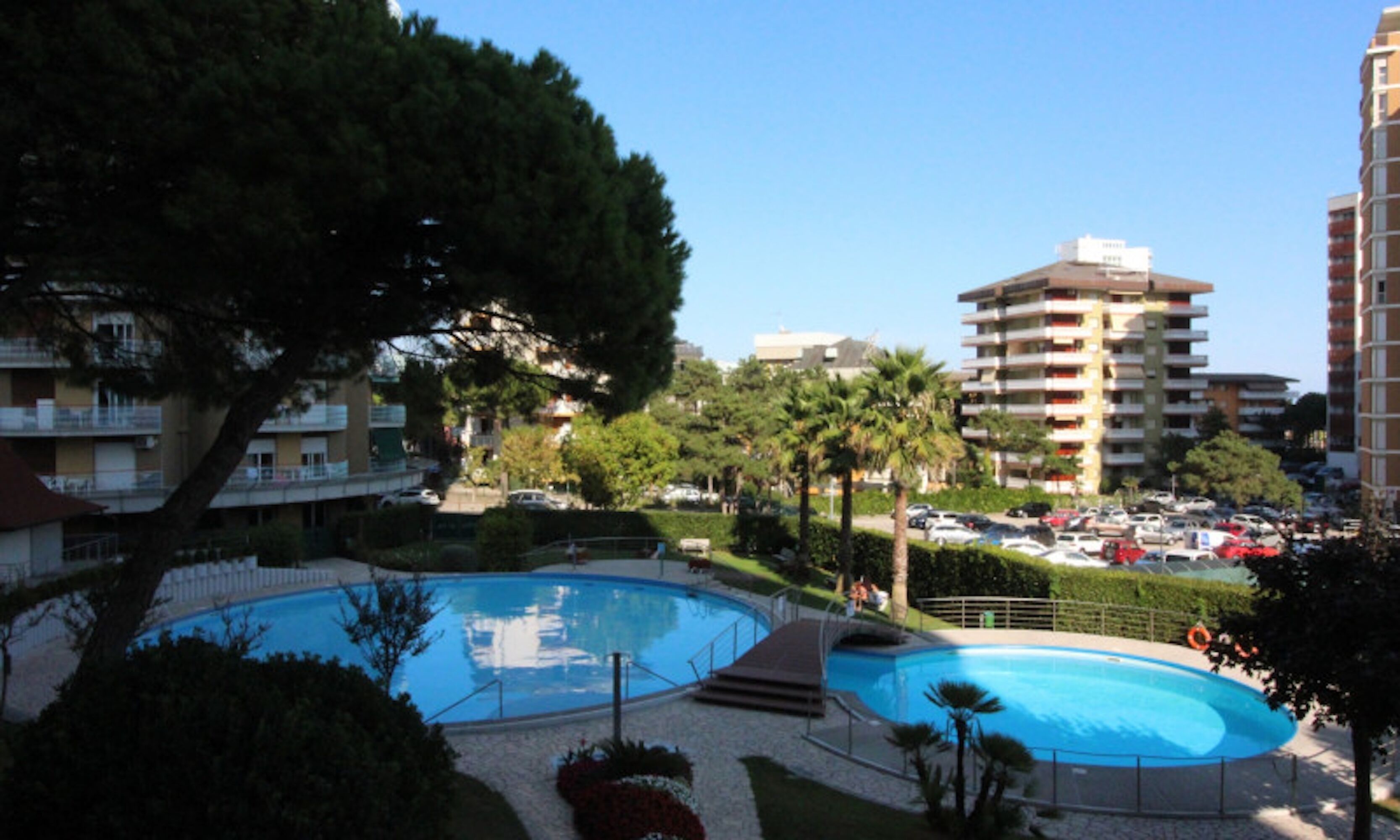 Zona residencial con piscina rodeada de vegetación y edificios altos al fondo.