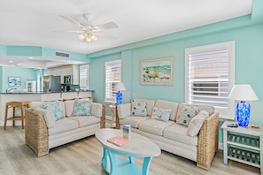 A living room with two sofas, a coffee table, wicker side tables, a ceiling fan, and a kitchen in the background. - Sun & Sea B200 - GULF FRONT (Indian Rocks Beach)