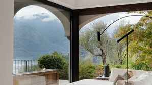 Un dormitorio moderno con un ventanal grande, un sofá, un atril de lectura y vistas a montañas.