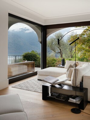 A modern bedroom with a large window, a sofa, a reading stand, and a view of mountains. - Villa Magnifica by My Villa Collection (Lenno)