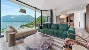 Un salón moderno con un sofá verde, una mesa de centro de mármol y vistas a montañas y un lago.