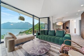 Ein modernes Wohnzimmer mit einem grünen Sofa, einem Marmortisch und Blick auf Berge und einen See.