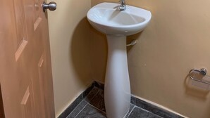 A bathroom with a white pedestal sink, a mirror above it, and a wooden door.
