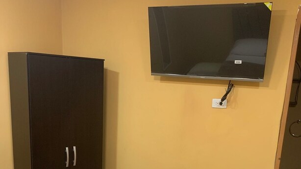 A bedroom with a bed, a wardrobe, and a television mounted on the wall.