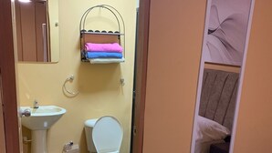 A compact bathroom with a toilet, sink, and a towel rack with folded towels.