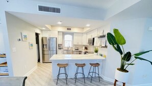Une cuisine moderne avec un îlot central, des tabourets de bar et une plante en pot.