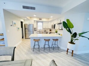 A modern kitchen with a central island, bar stools, and a potted plant. - Sun and Sea C2 - Coastal Luxury (Indian Rocks Beach)