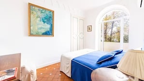 Ein Schlafzimmer mit Bett, einem Gemälde, einem Fenster und einer Lampe.