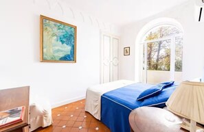 Ein Schlafzimmer mit Bett, einem Gemälde, einem Fenster und einer Lampe.