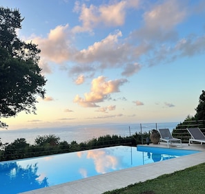 Ein Schwimmbad mit Blick auf das Meer und einen Sonnenuntergang.