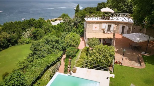 Ein zweistöckiges Haus mit Pool, umgeben von üppiger Vegetation und mit Blick auf ein Gewässer.