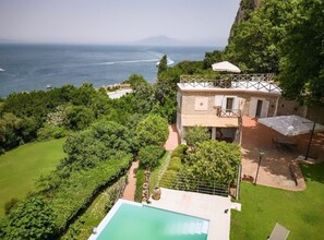 Une maison à deux étages avec une piscine, entourée d’une végétation luxuriante et offrant une vue sur un plan d’eau.
