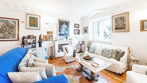 Ein Wohnzimmer mit blauem Sofa, weißen Sesseln, einem Couchtisch und Kunstwerken an den Wänden.