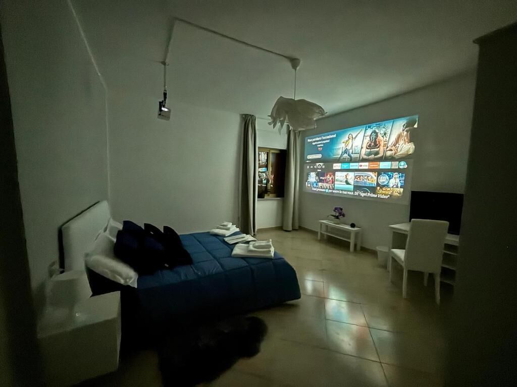 Habitación de hotel moderna con cama, escritorio, silla y un televisor grande de pared que muestra una película.