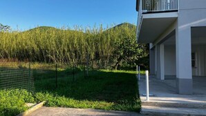 Un bâtiment moderne doté d’un balcon, d’une zone pavée et d’un terrain herbeux délimité par une clôture.