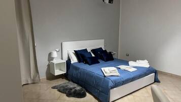 A bedroom with a bed, white nightstands, a lamp, and a ceiling-mounted projector.