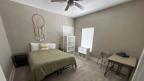 Un dormitorio con cama, escritorio, silla, armario y ventilador de techo.