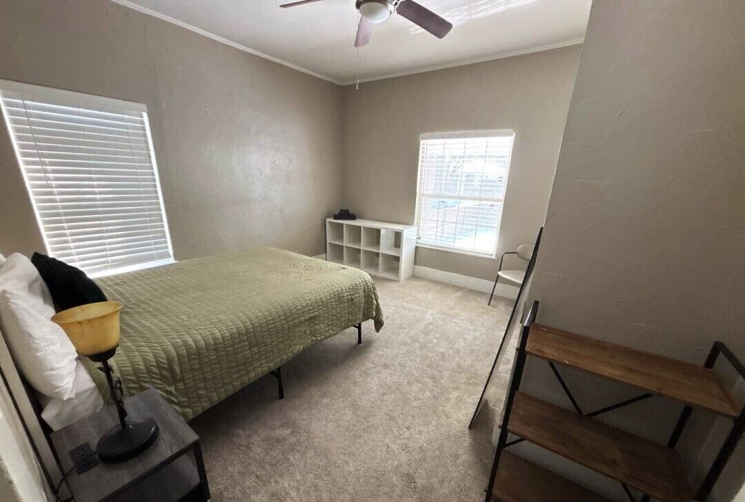 A bedroom with a bed, bedside table, lamp, window, and built-in shelving unit.