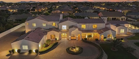 A large, multi-story residential building with a driveway, landscaped garden, and multiple entry points.