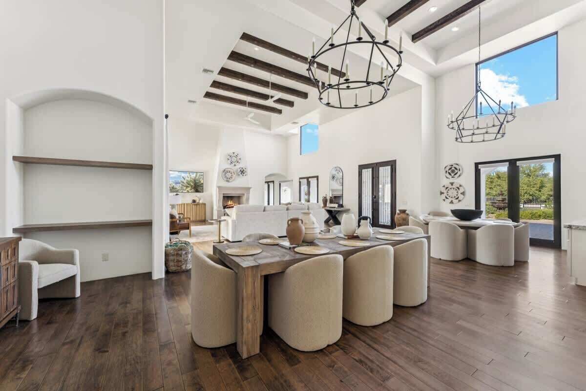 A spacious living area with a large wooden dining table, comfortable seating, and a modern chandelier.