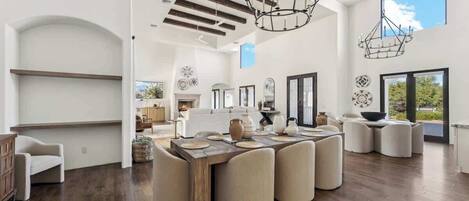A spacious living area with a large wooden dining table, comfortable seating, and a modern chandelier.