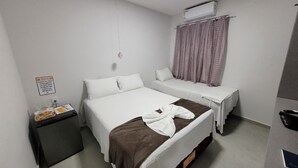 Ein Hotelzimmer mit zwei Betten, einem kleinen Nachttisch mit Lampe, einer Wandklimaanlage und einem Fenster mit Vorhängen.