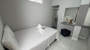 Ein modernes Schlafzimmer mit einem großen Bett, einem schwarzen Hocker, einem Spiegel und einem kleinen Regal mit Dekorationen.