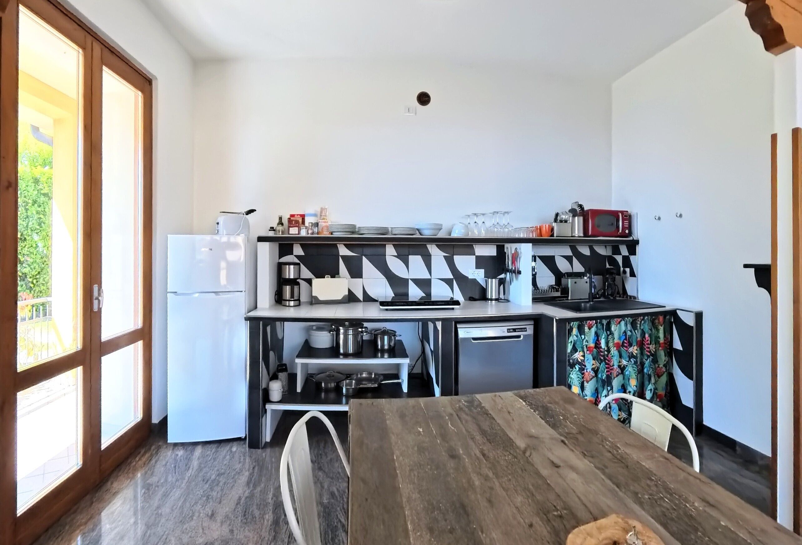 A compact kitchen with a refrigerator, microwave, and coffee maker. A dining table is in the foreground with chairs.