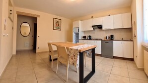 A compact kitchen with white cabinets, a dining table with chairs, and a tiled floor. - Villa Arianna (Gardola)
