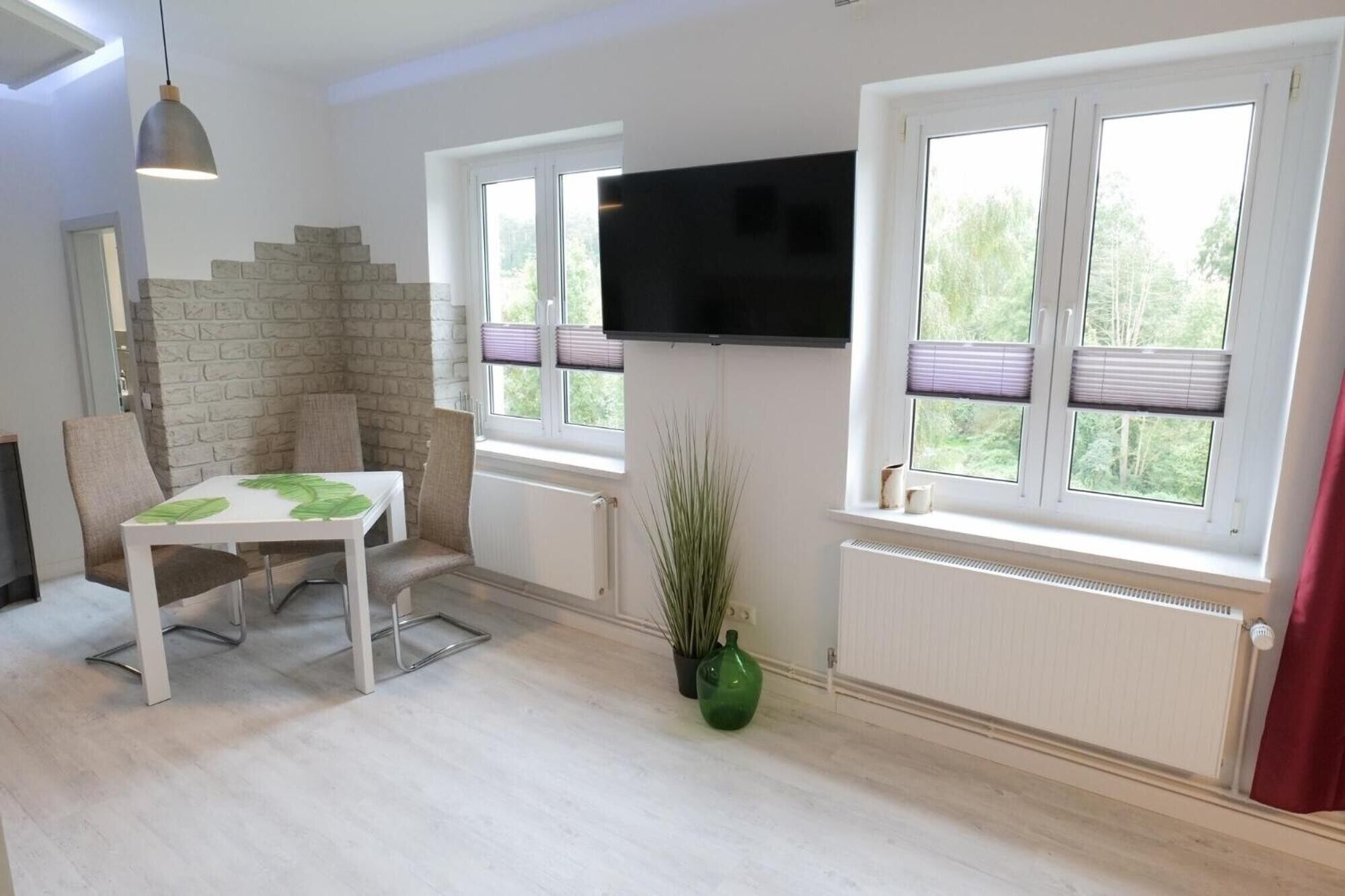 A room with a white table and chairs, a TV mounted on the wall, and windows with blinds.