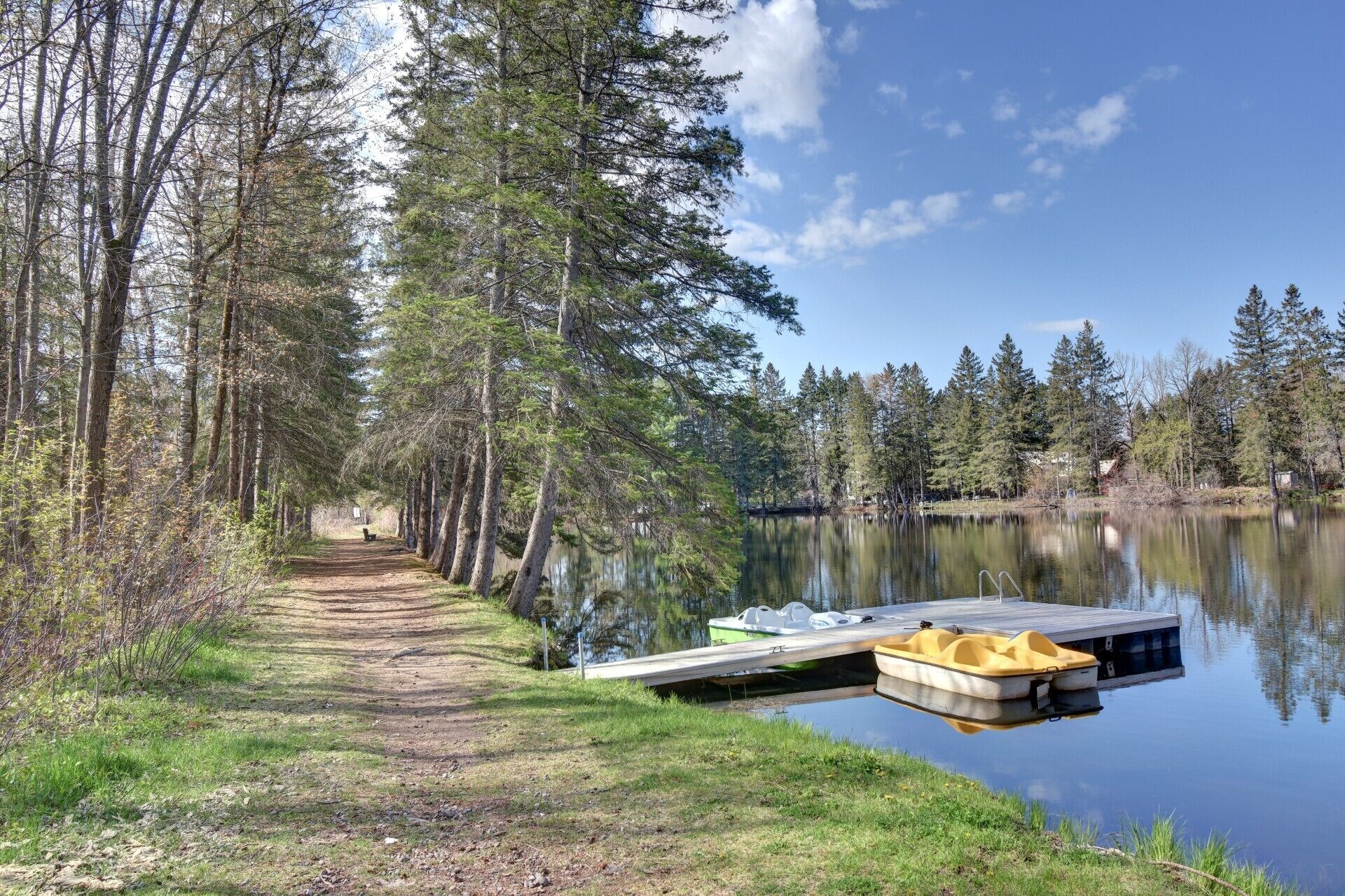 A tranquil lakeside path with a dock and a yellow boat.