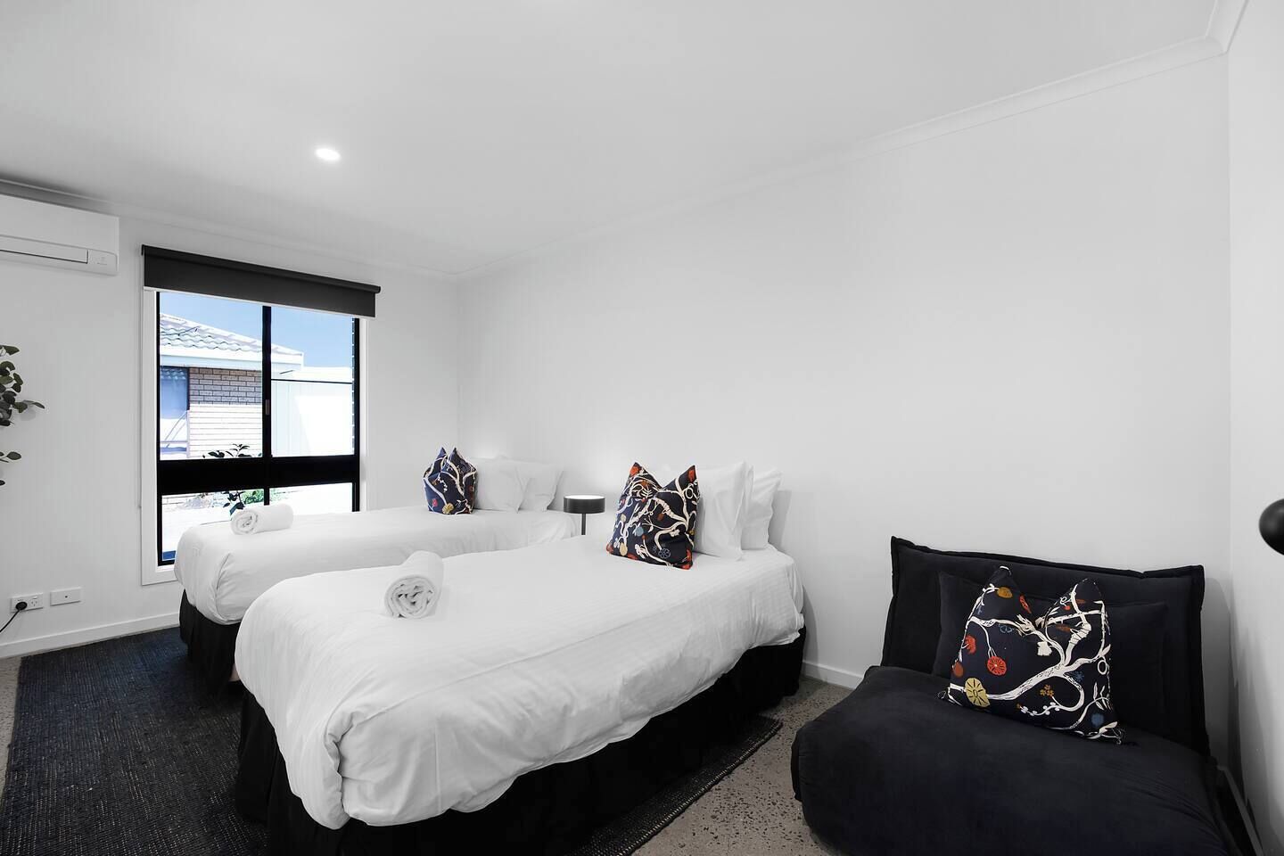 Une chambre d’hôtel avec deux lits, un canapé noir et une fenêtre donnant sur un immeuble.