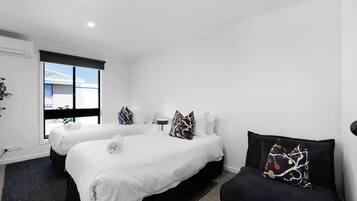 Une chambre d’hôtel avec deux lits, un canapé noir et une fenêtre donnant sur un immeuble.