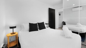 Ein modernes Hotelzimmer mit einem großen Bett, einem Nachttisch mit Lampe, einem Kleiderschrank und einem Spiegel.