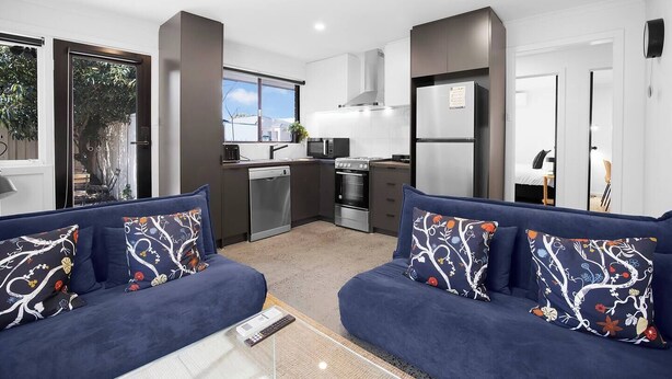 Eine moderne Wohnung mit Küche, zwei Sofas mit gemusterten Kissen und Blick ins Freie.
