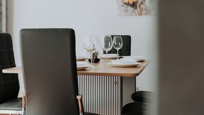 Un coin repas avec une table en bois dressée pour deux personnes, agrémentée de verres à vin en verre transparent et d’assiettes blanches.