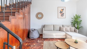 Un salon moderne avec un escalier en bois, un fauteuil poire gris, un canapé beige, une table basse ronde et une plante en pot.