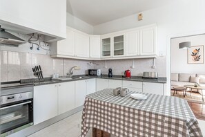 Une cuisine moderne avec des meubles blancs, une nappe à carreaux et un coin repas comprenant un canapé et une table basse.