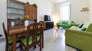 Uma sala de estar moderna com uma mesa de jantar de madeira, sofá verde e uma televisão.
