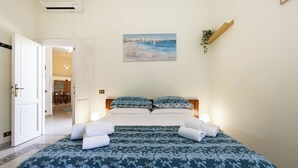 Quarto com cama, almofadas e uma pintura de uma praia.