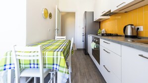 Uma cozinha compacta com armários brancos, uma geladeira de aço inoxidável e um revestimento de azulejos amarelos.