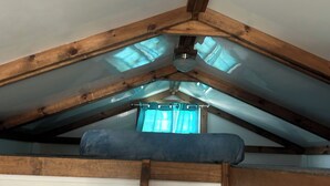 Een slaapkamer in een loft met een schuin dak, een houten trapje en een bed met een blauwe deken.