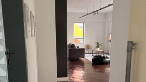 A hallway with a dark wooden floor, a grey wall, and a white door on the left. There is a window with a yellow and orange design on the wall, and a plant on a small table in the background. - A spacious loft in the heart of the Maboneng Precinct, Johannesburg (Johannesburg)