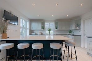 Una cocina moderna con una isla grande, taburetes de bar, muebles blancos y un televisor de pantalla plana.