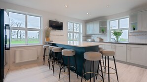 Una cocina moderna con una isla central, taburetes de bar, un televisor de pantalla plana y ventanas amplias.