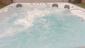 Un jacuzzi con múltiples chorros, rodeado por un muro de ladrillo y una zona verde.